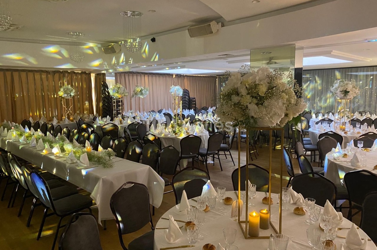 Salle de réception décorée pour un événement, avec tables dressées, nappes blanches, chandelles et compositions florales.