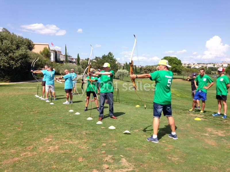 Groupe d'enfants en tenue sportive pratiquant le tir à l'arc en plein air sur un terrain herbeux.