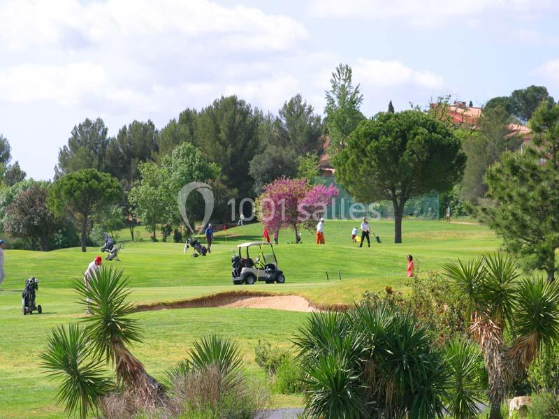 Parcours de golf avec bunker en sable, golfeurs et chariot motorisé sur fairway arborisé, palmiers et bâtiments en arrière-plan.