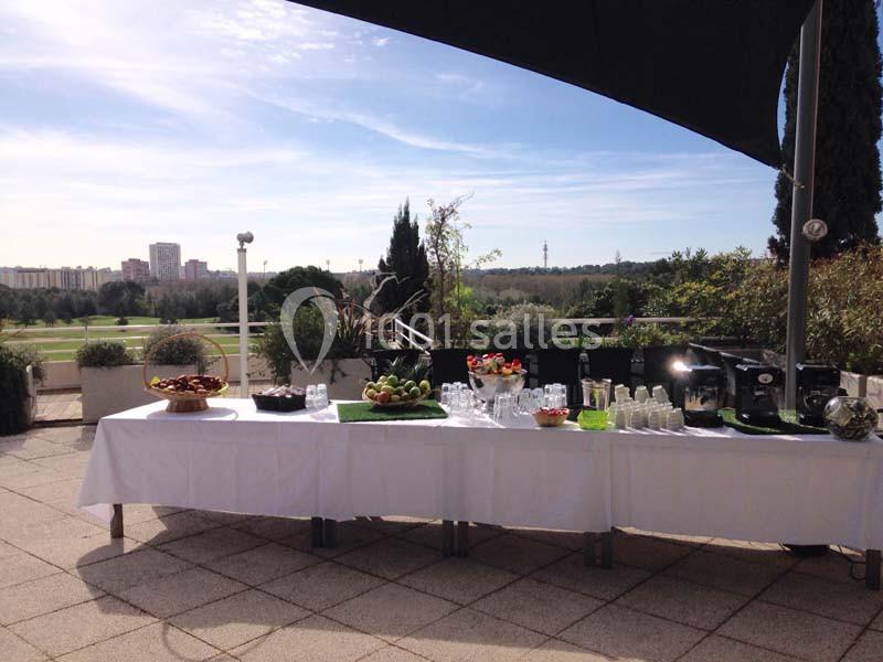 Terrasse couverte avec table dressée face à un parcours de golf et vue sur les collines boisées.