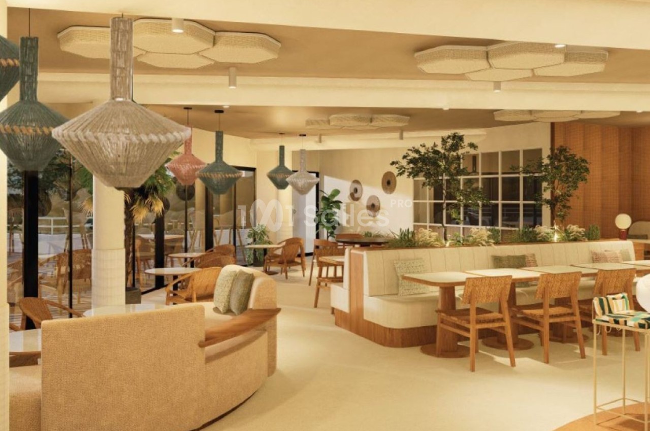 Espace intérieur lumineux avec mobilier en bois clair, tables dressées, canapé, lampes suspendues géométriques et plantes vertes.