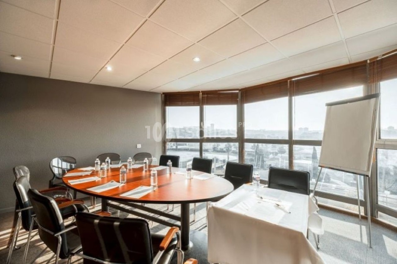Salle de réunion avec table ovale orange, chaises noires, baies vitrées panoramiques sur la ville et écran de projection.