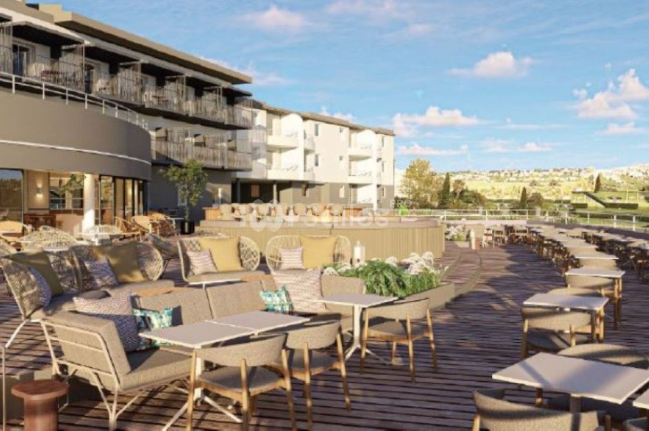 Terrasse aménagée avec fauteuils et tables basses, vue sur bâtiments modernes et paysage vallonné.