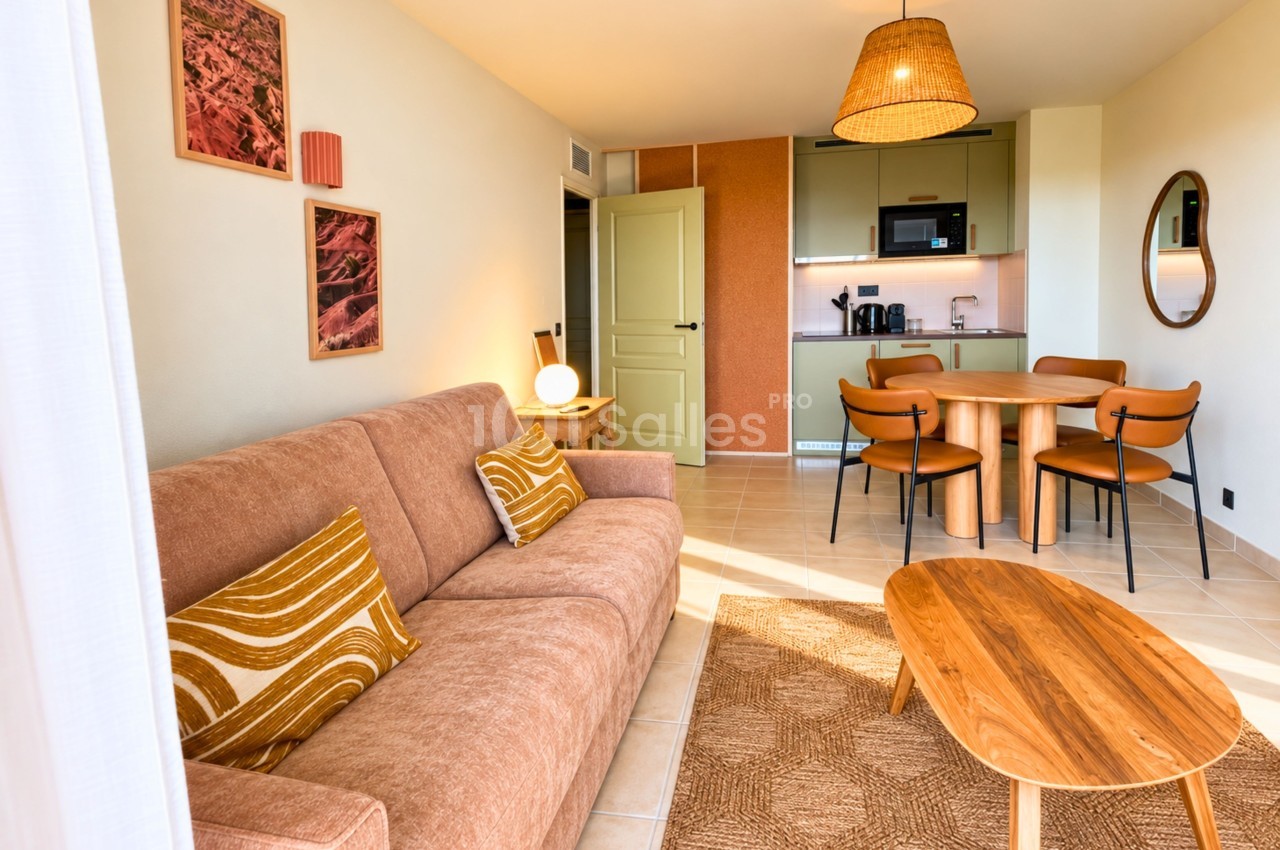 Intérieur d'un espace ouvert avec canapé rose, table basse en bois, cuisine aménagée et table de salle à manger.