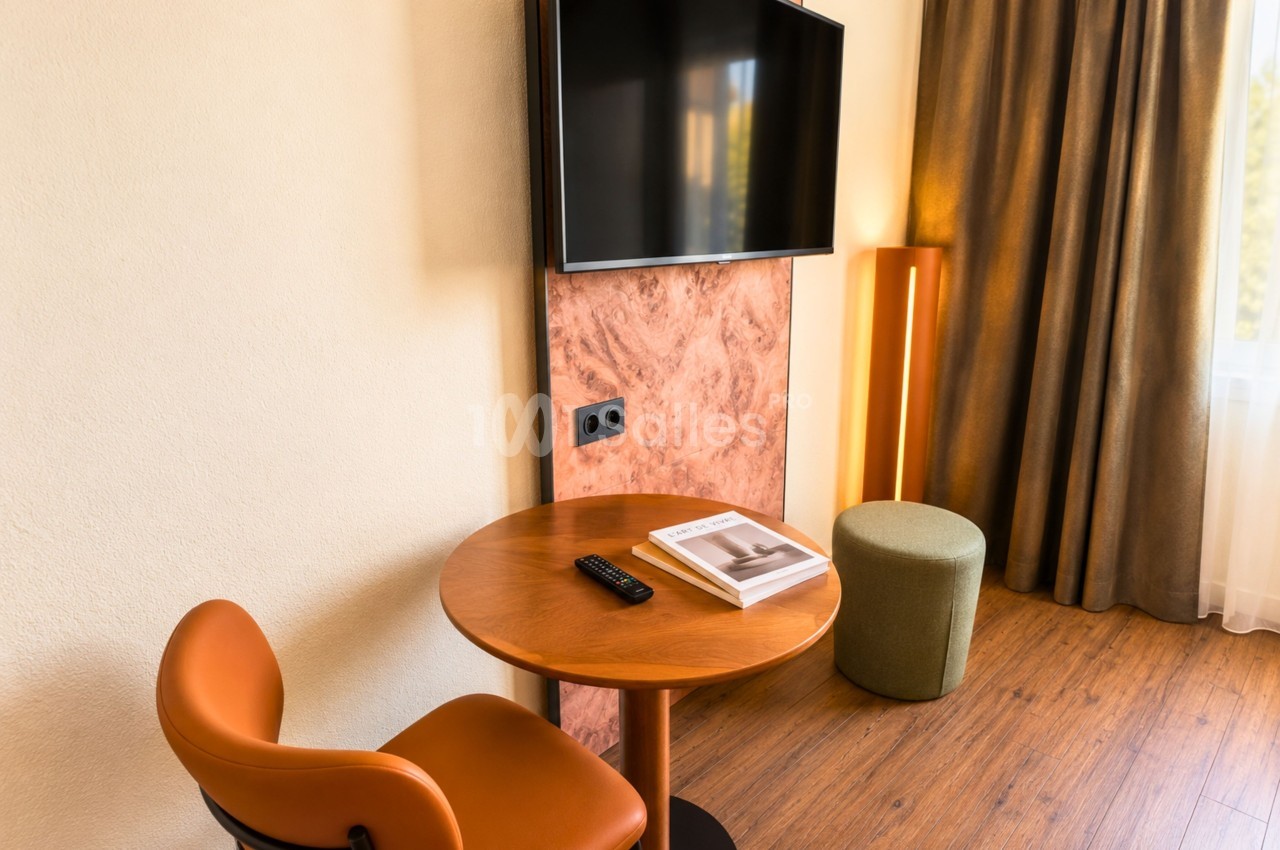 Coin détente avec fauteuil orange, table basse ronde en bois, pouf, téléviseur mural et panneaux rose terracotta.