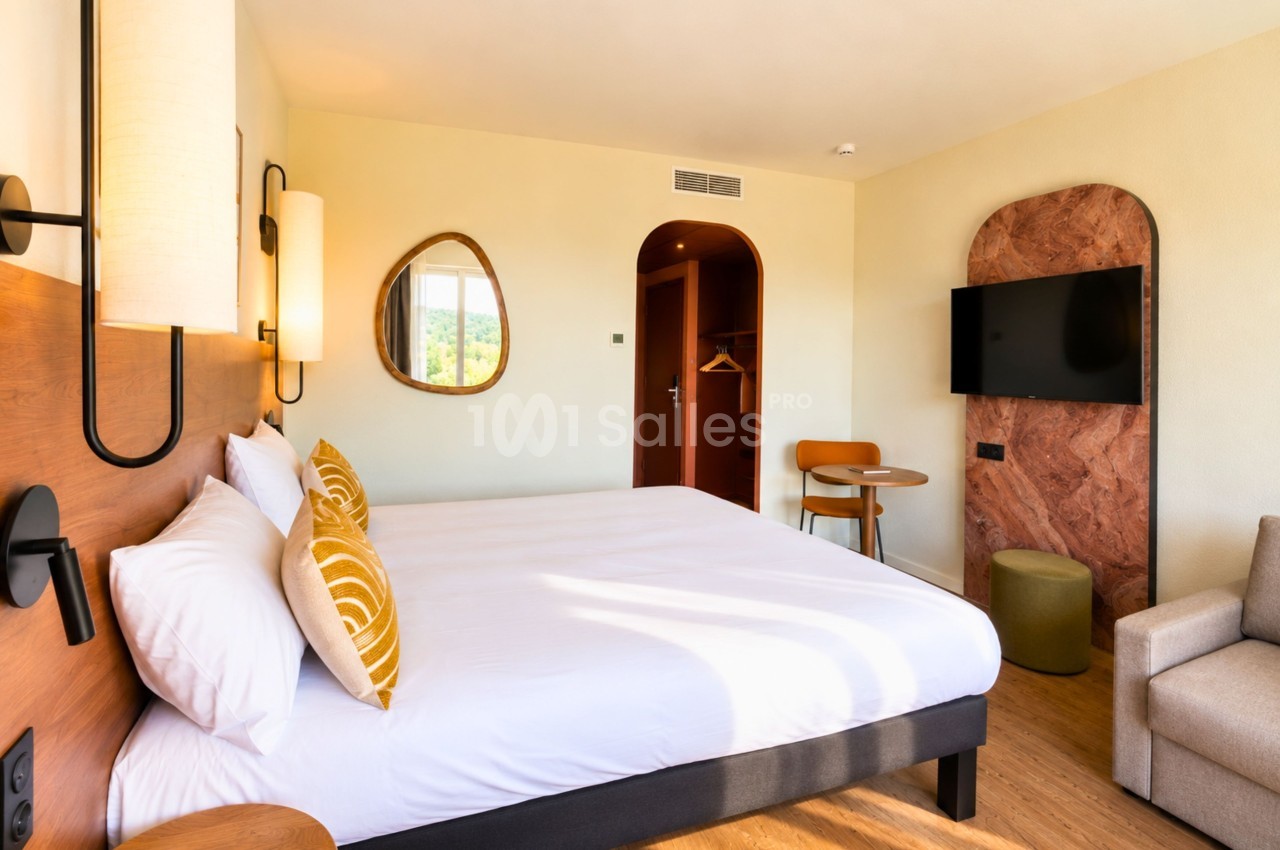 Chambre d'hôtel avec lit double, tête de lit bois, miroir ovale, télévision murale et mobilier moderne.