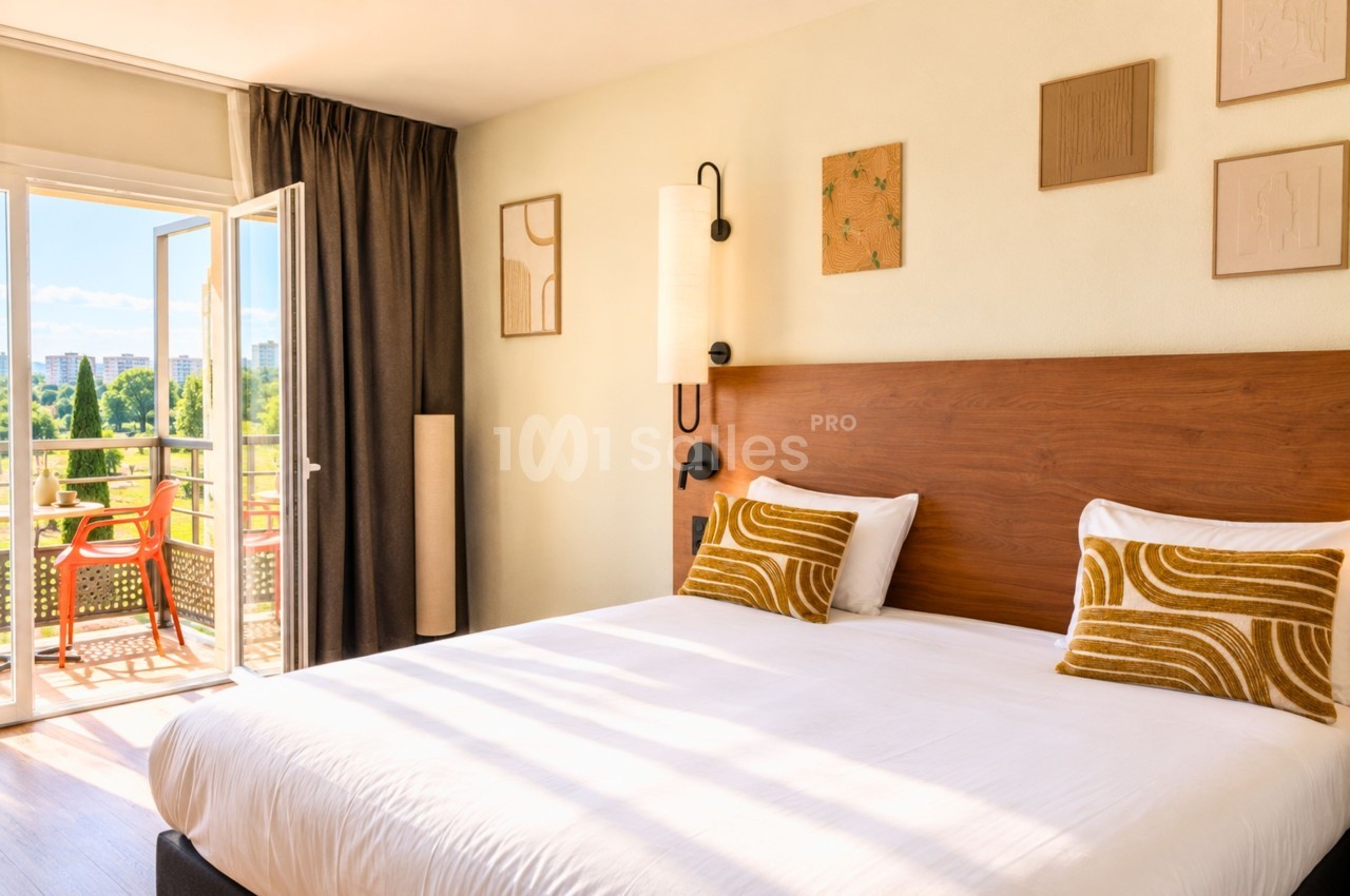 Chambre double avec lit en bois, coussins jaunes, baies vitrées ouvrant sur balcon et vue urbaine.