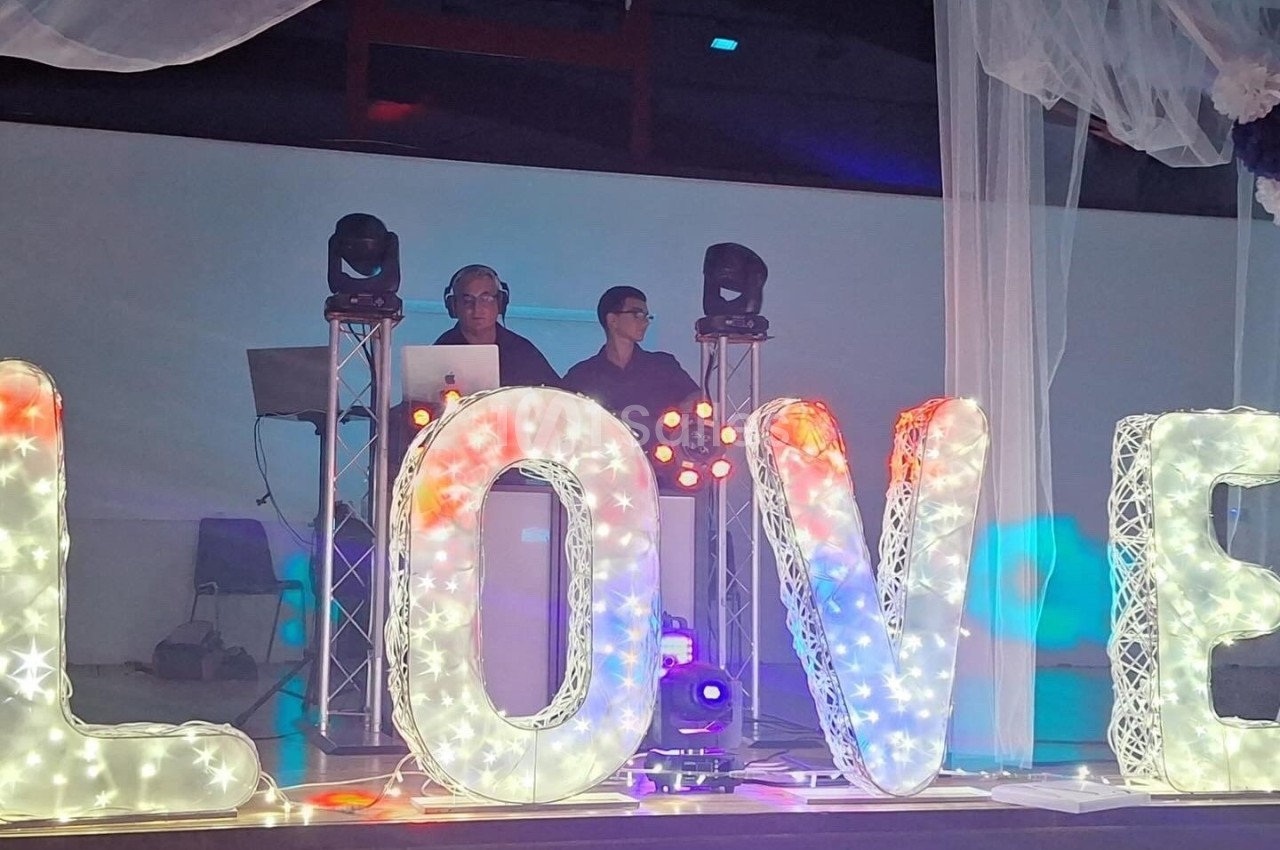 Deux DJ derrière une table de mixage, entourés de grandes lettres lumineuses formant le mot ’LOVE’.