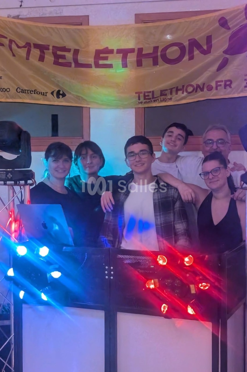 Un groupe de personnes souriantes posant devant une bannière du Téléthon, entourées d'équipements lumineux.