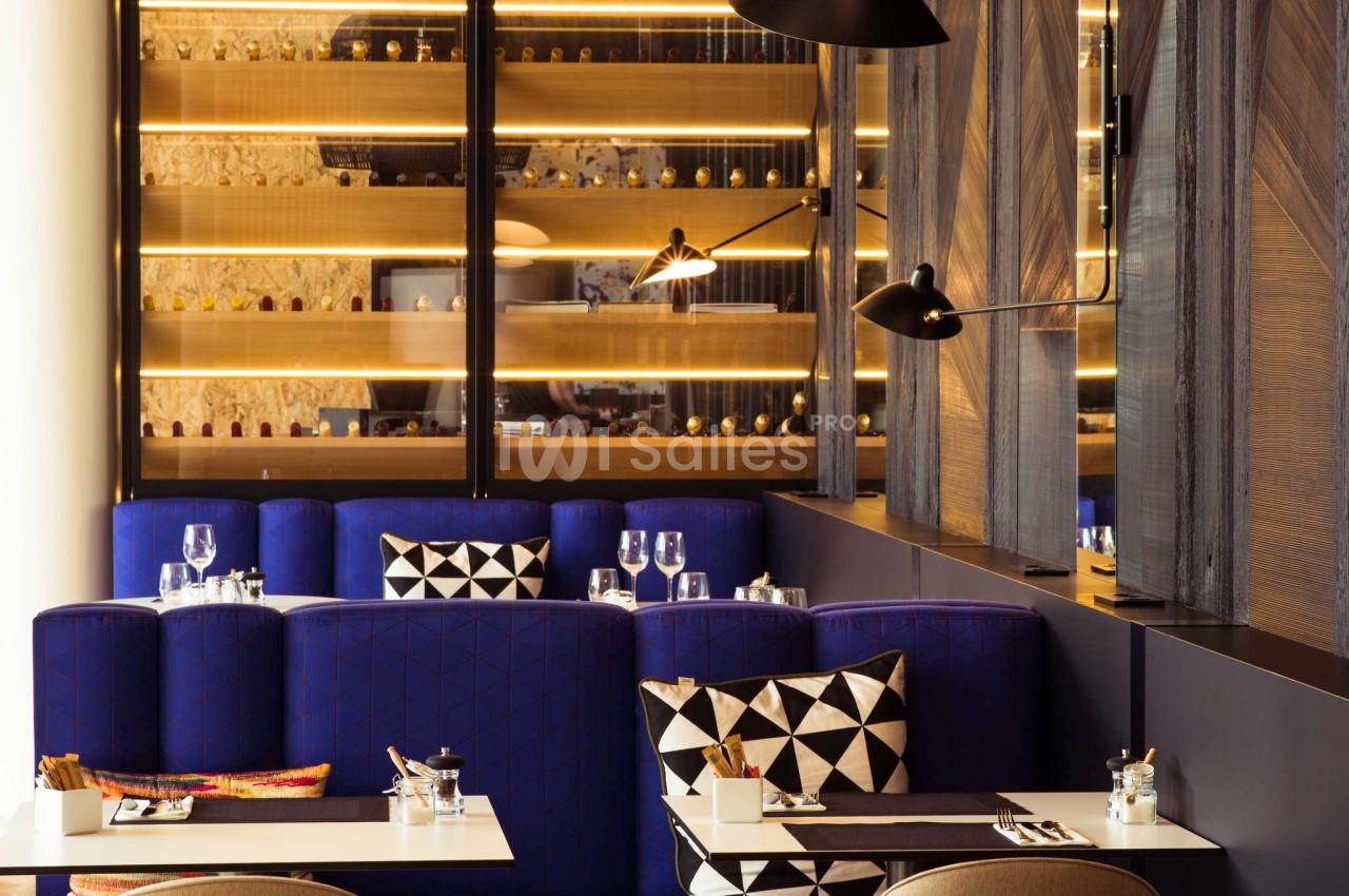 Banquettes bleues avec coussins géométriques dans un restaurant moderne, éclairé par des étagères lumineuses en arrière-plan.