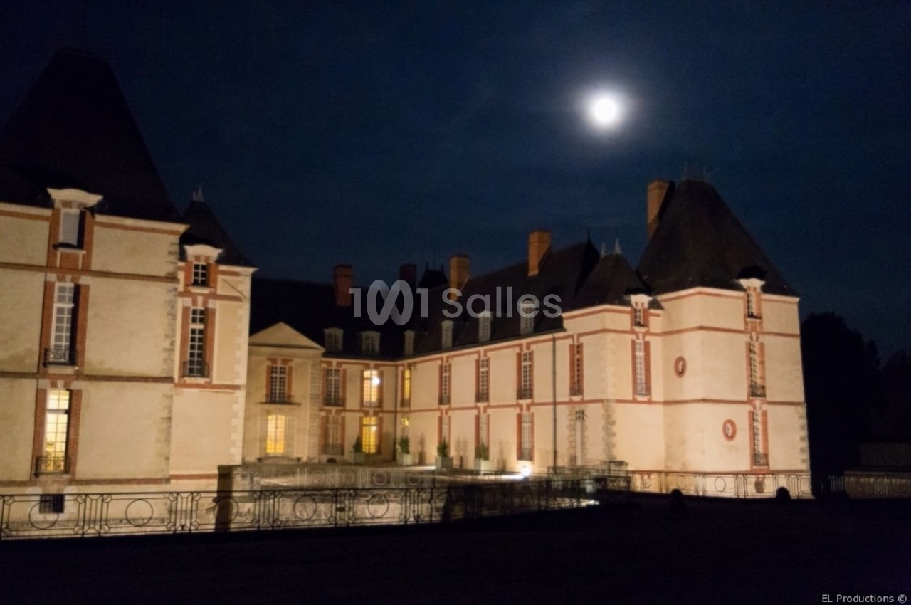 Château éclairé sous un ciel nocturne avec une pleine lune visible en arrière-plan.