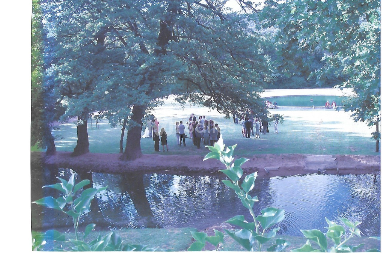 Groupe de personnes rassemblées dans un parc verdoyant près d'un étang, entouré d'arbres et de pelouse.