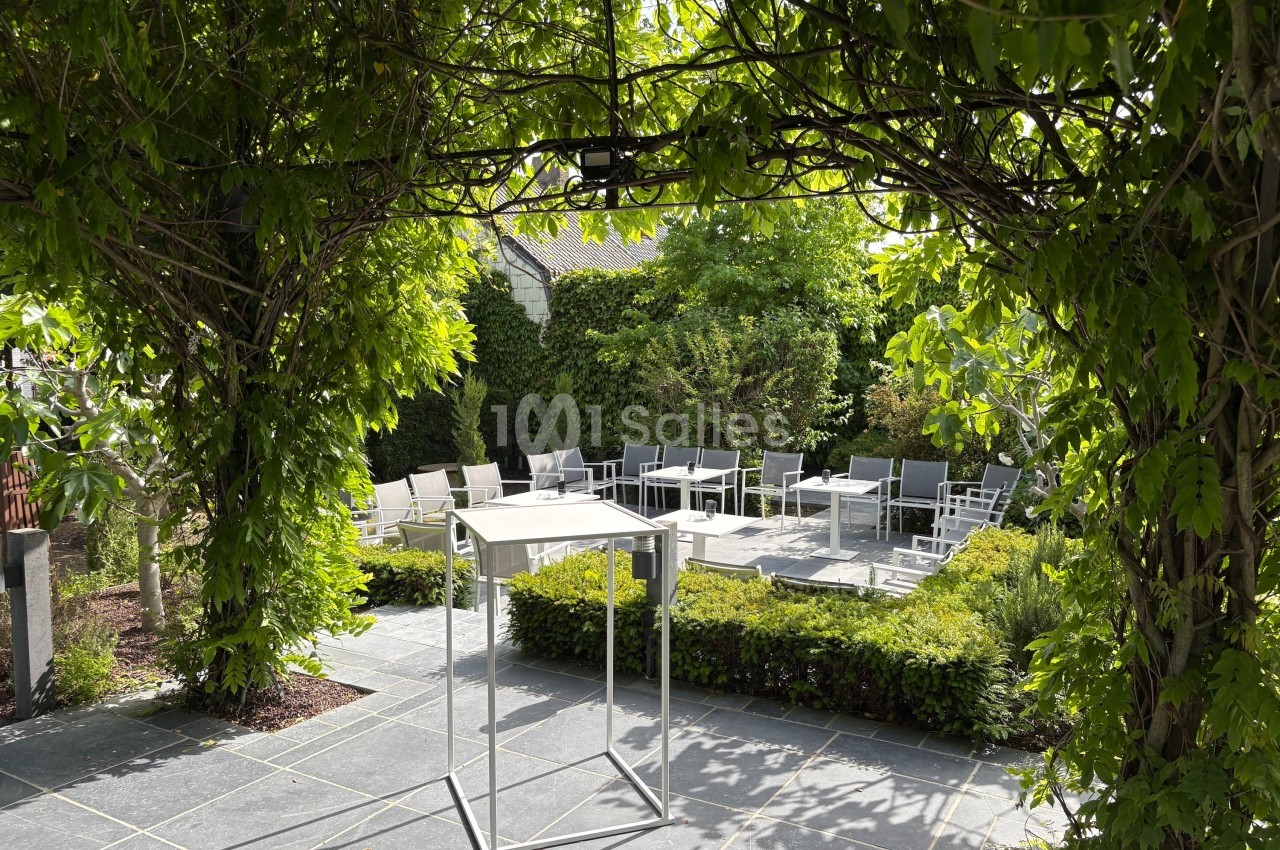 Terrasse extérieure ombragée avec des tables et des chaises entourées de végétation verdoyante.