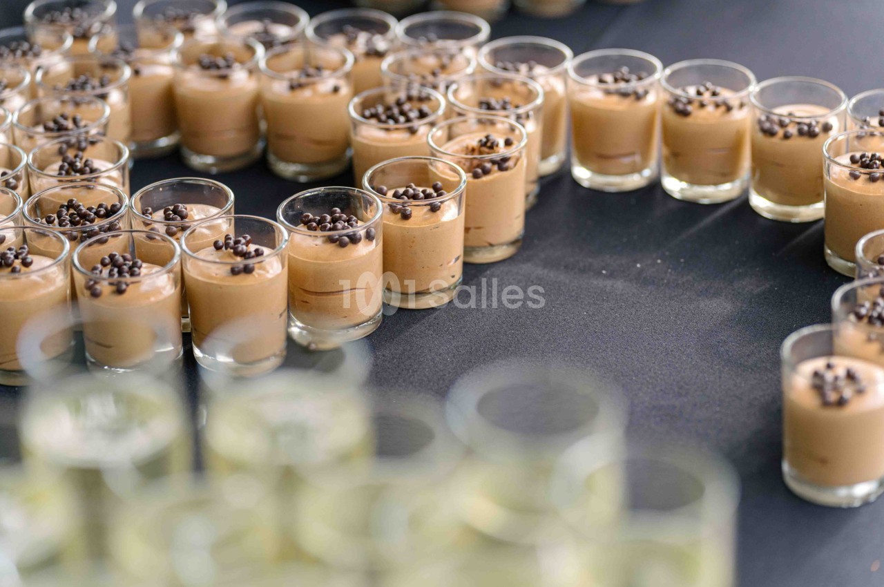 Petits verres de mousse au chocolat garnis de pépites de chocolat, disposés en cercle sur une table noire.