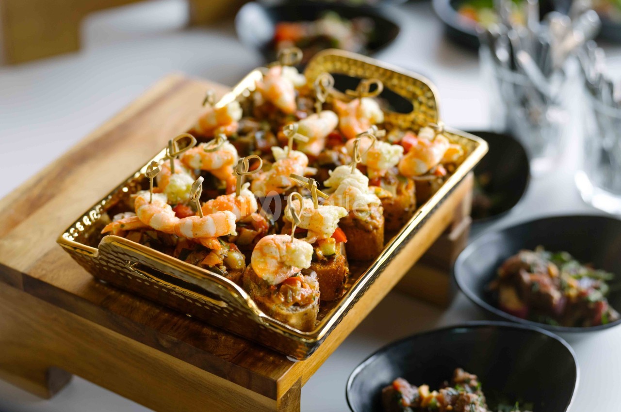 Plateau doré contenant des bouchées apéritives garnies de crevettes et de légumes, présenté sur une table.