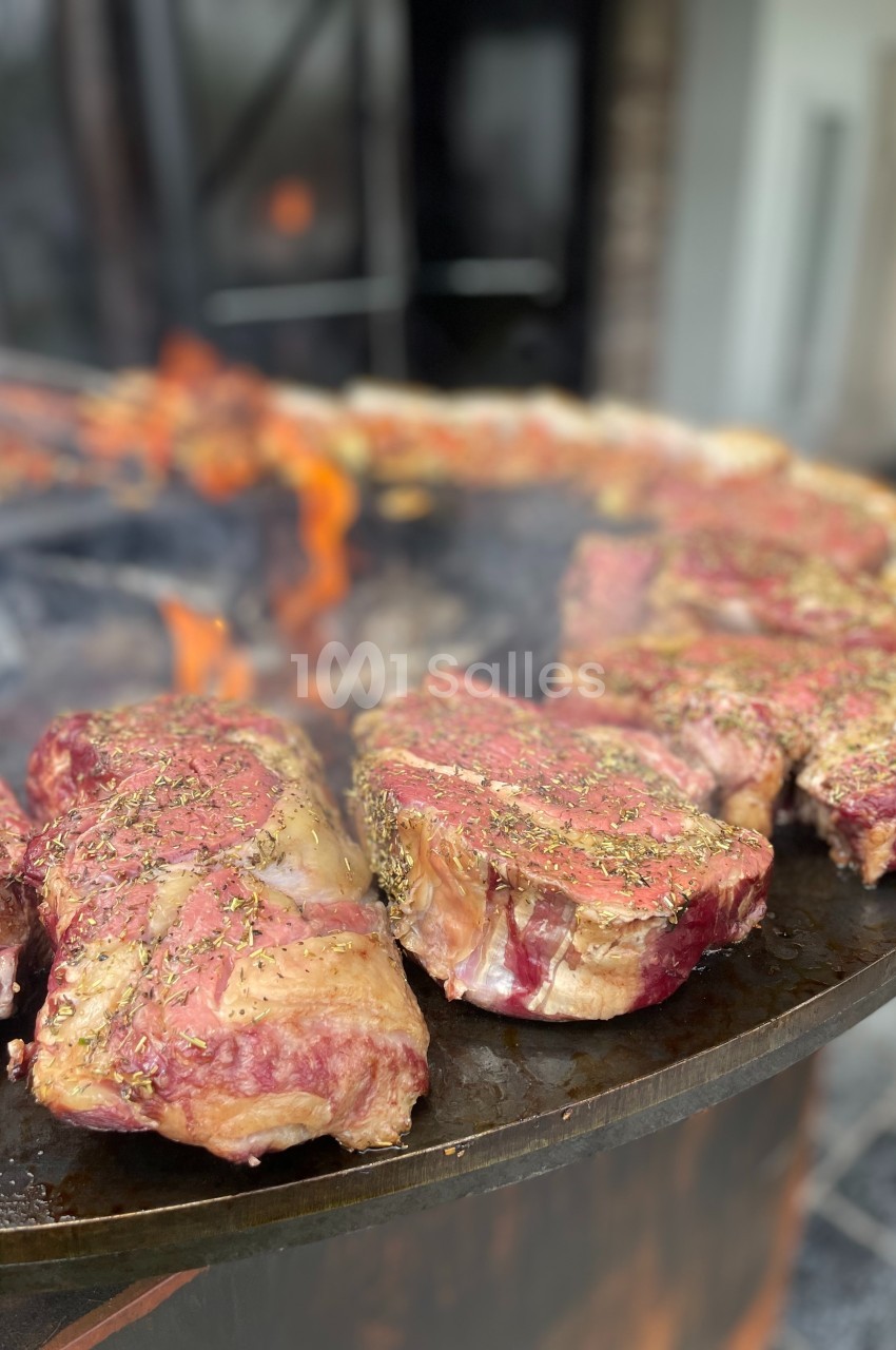 Viande rouge assaisonnée en train de griller sur une plaque chauffante au-dessus d'un feu de bois.