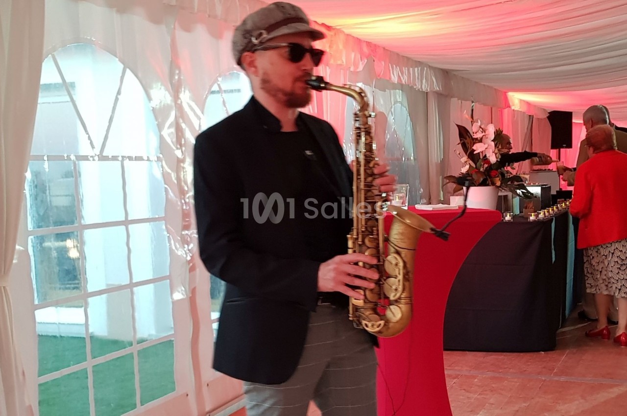 Un musicien joue du saxophone dans une tente éclairée de lumières rouges lors d'un événement.