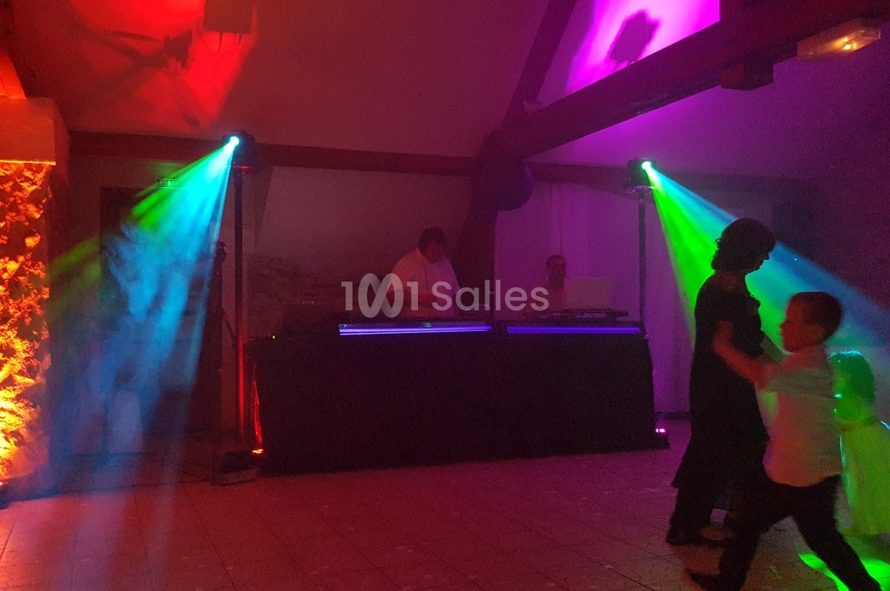 Personnes dansant devant un DJ avec des jeux de lumière colorés dans une salle sombre.