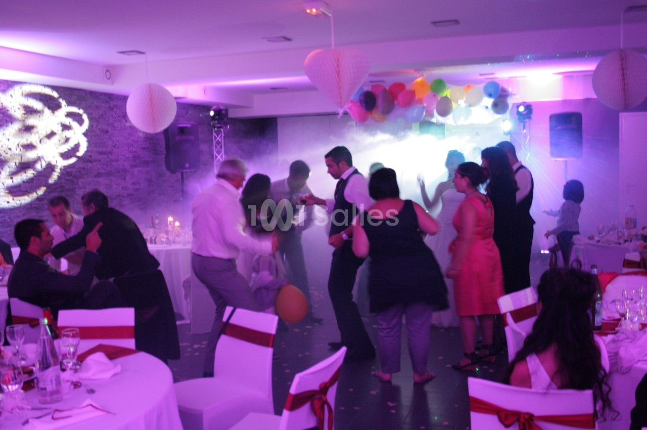 Des personnes dansent dans une salle décorée avec des lumières colorées, des ballons et des guirlandes suspendues.