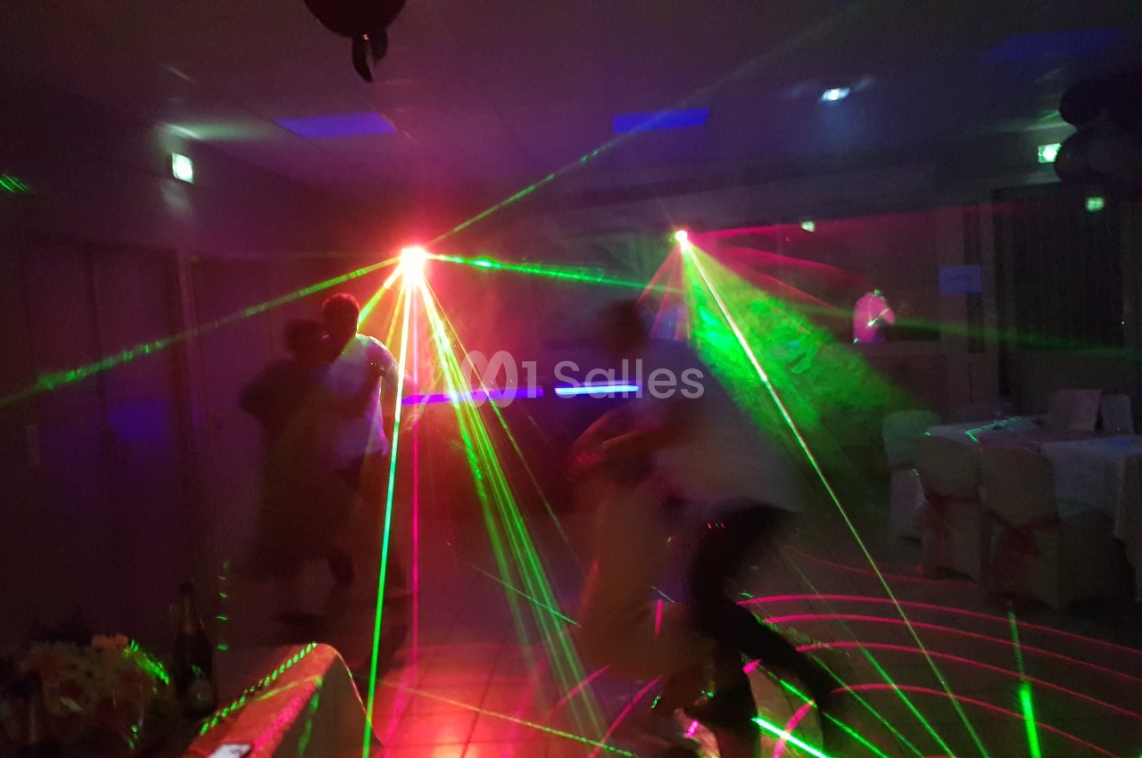 Des personnes dansent dans une salle sombre éclairée par des faisceaux lumineux colorés et des effets laser.