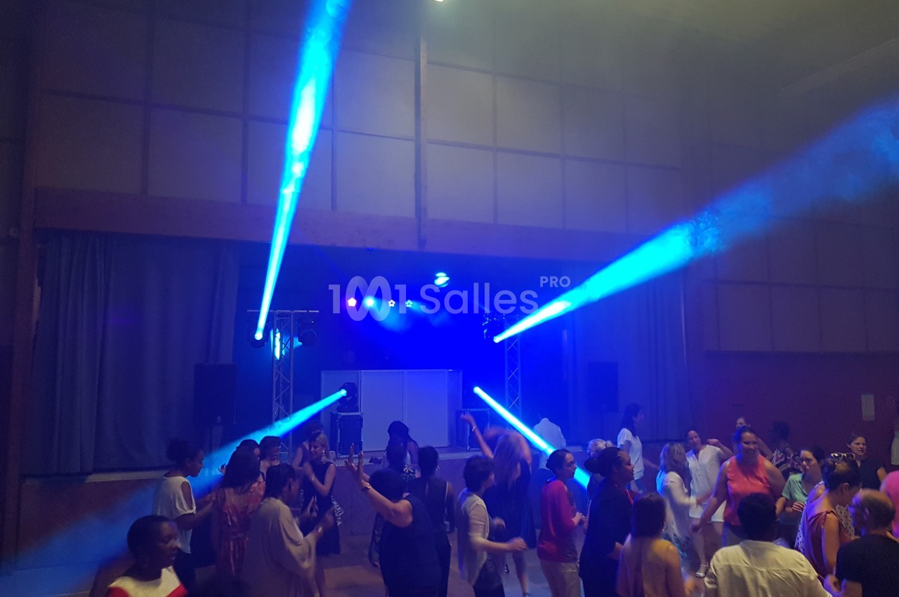 Des personnes dansent dans une salle éclairée par des projecteurs bleus, créant une ambiance festive.