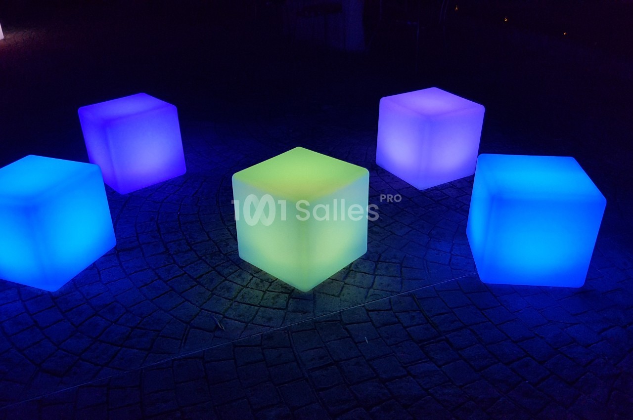 Cubes lumineux colorés posés sur un sol pavé, éclairés dans l'obscurité.
