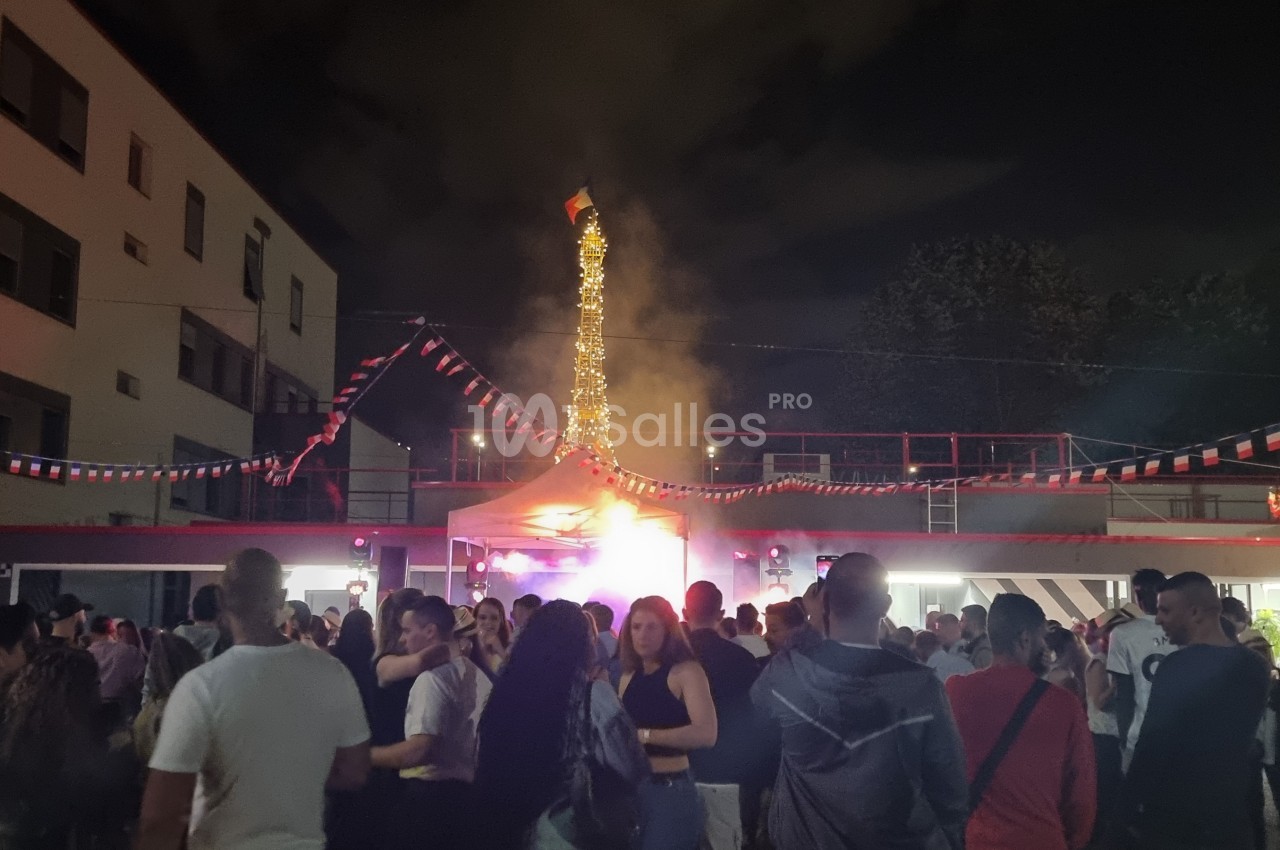 Foule rassemblée de nuit dans une cour décorée de guirlandes, avec une structure illuminée en arrière-plan.