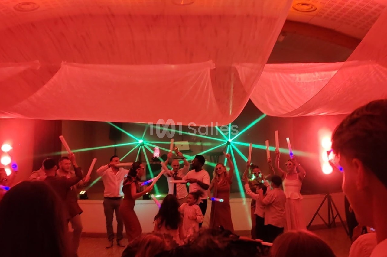 Des personnes dansent sous des lumières colorées et des lasers lors d'une fête ou d'un événement festif en intérieur.