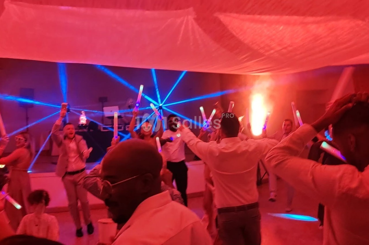 Des personnes dansent sous des lumières colorées avec des bâtons lumineux dans une salle décorée.