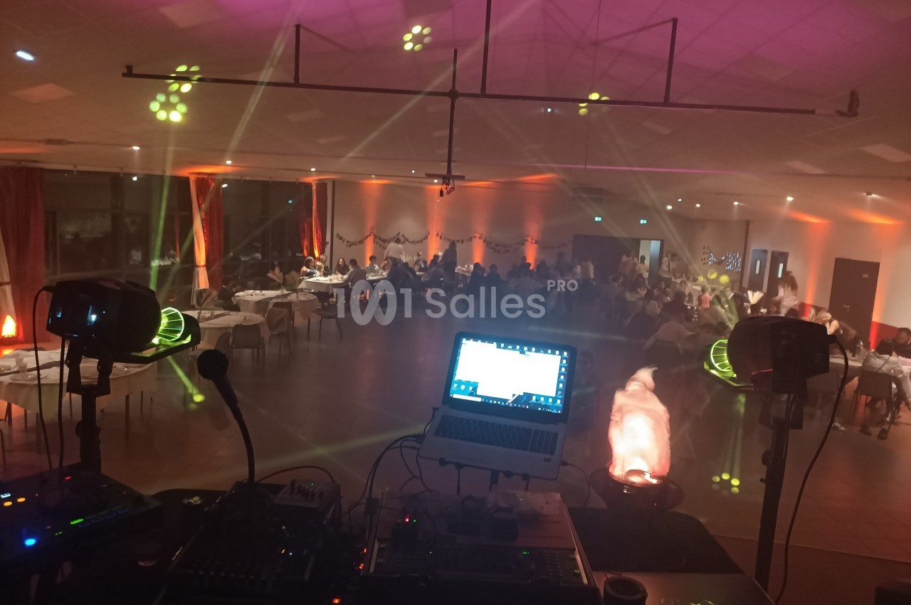 Vue depuis une table de DJ avec éclairages colorés et invités assis dans une salle de réception décorée.