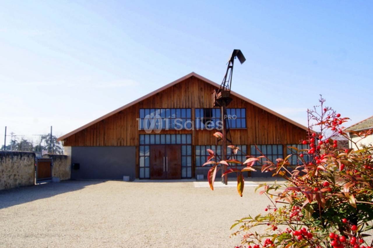 Bâtiment en bois avec de grandes baies vitrées, une grue ancienne devant et des arbustes rouges au premier plan.