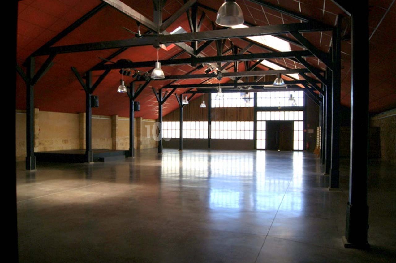 Intérieur d'un grand espace industriel rénové avec charpente apparente, sol en béton poli et lumière naturelle.