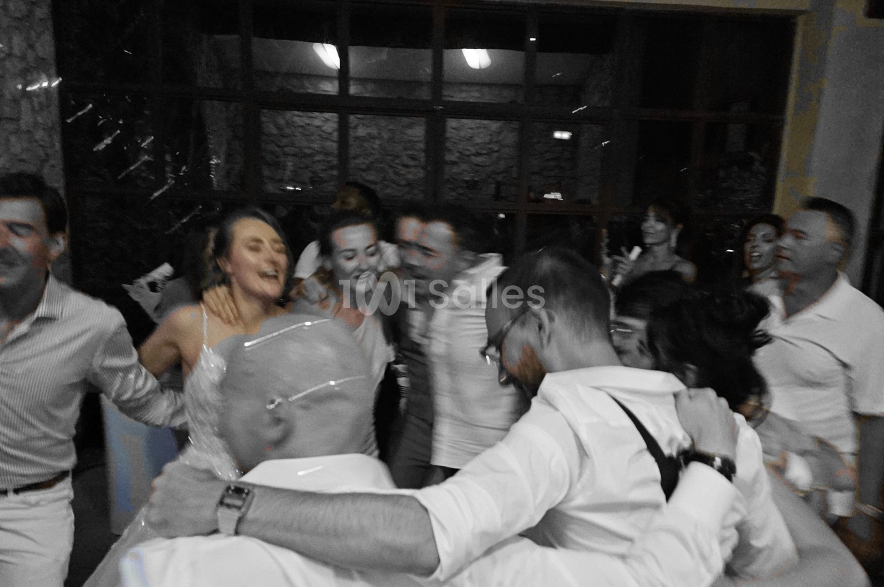 Des personnes dansent en cercle, souriantes et enlacées, dans une ambiance festive à l'intérieur d'une salle.