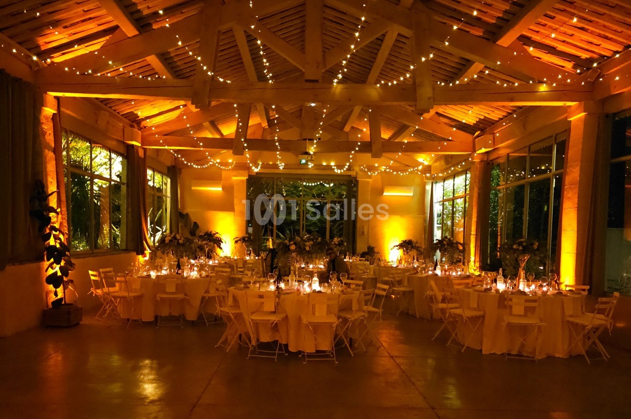 Salle de réception décorée avec des guirlandes lumineuses, des tables rondes dressées et une ambiance chaleureuse.