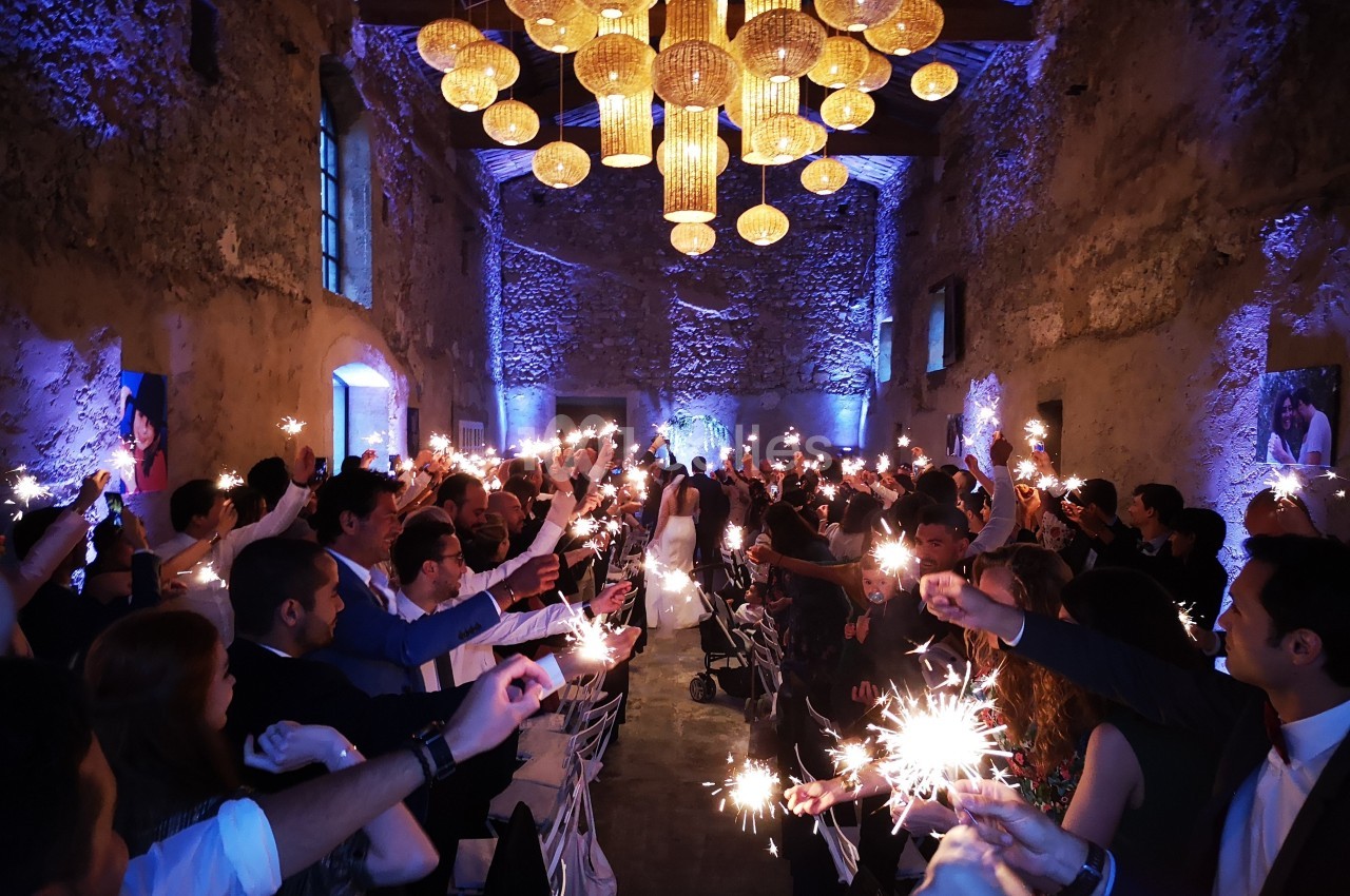 Des invités brandissent des cierges magiques allumés dans une salle en pierre illuminée pour une célébration festive.