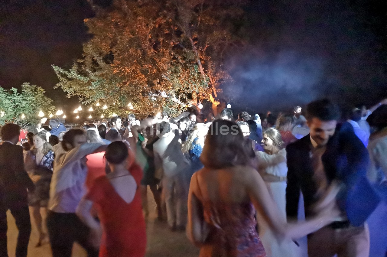 Groupe de personnes dansant en soirée en plein air, éclairées par des guirlandes lumineuses et des projecteurs.