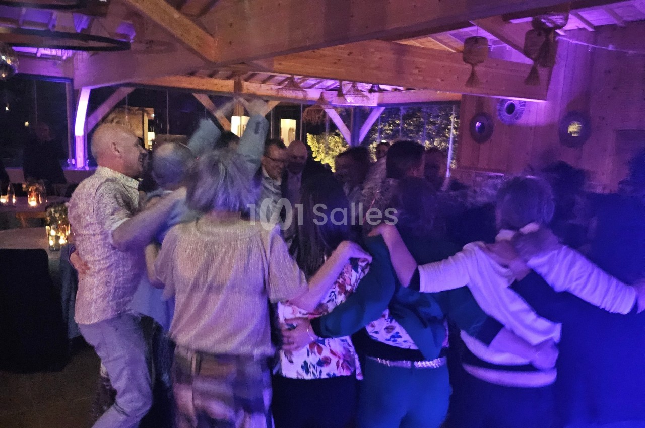 Groupe de personnes dansant en cercle dans une salle en bois éclairée par des lumières tamisées.