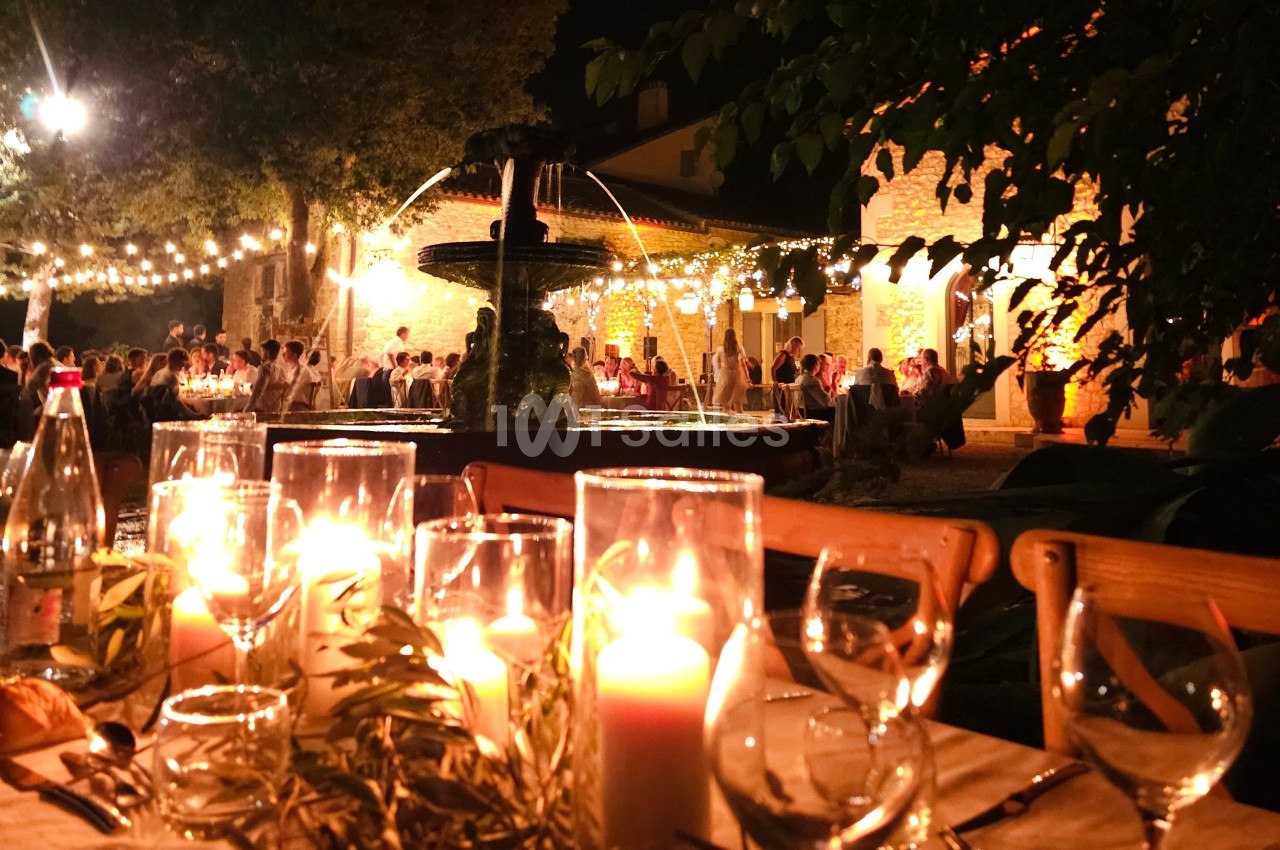 Table décorée avec des bougies allumées en premier plan, devant une fontaine éclairée et une réception en soirée.