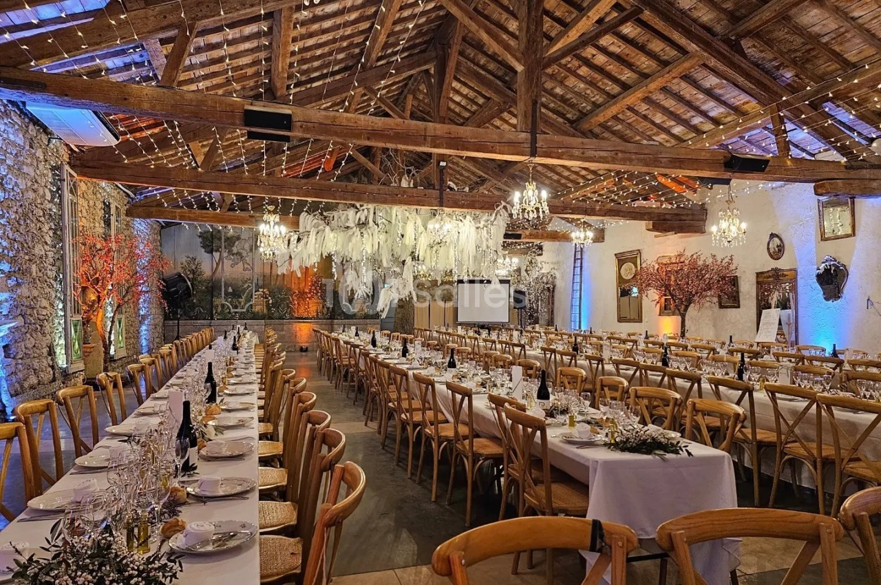 Grande salle de réception rustique avec tables dressées, chaises en bois, décorations lumineuses et plafond en poutres…