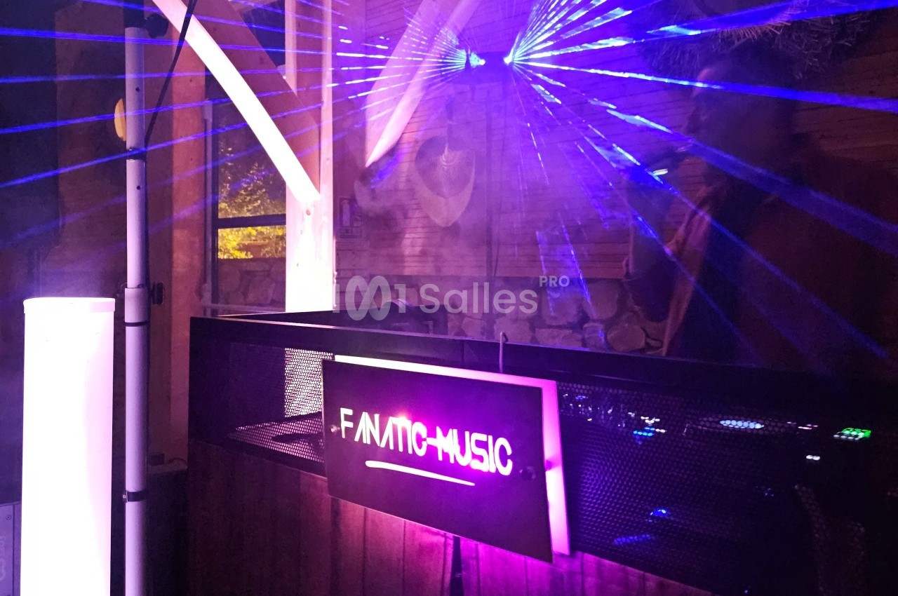 Poste de DJ éclairé par des lasers violets dans un espace intérieur avec un panneau ’F-AMIC MUSIC’.