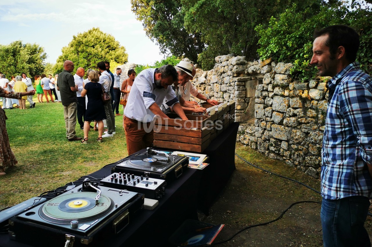 Des personnes participent à un événement en plein air près d'une table avec des platines vinyles et des caisses en bois.
