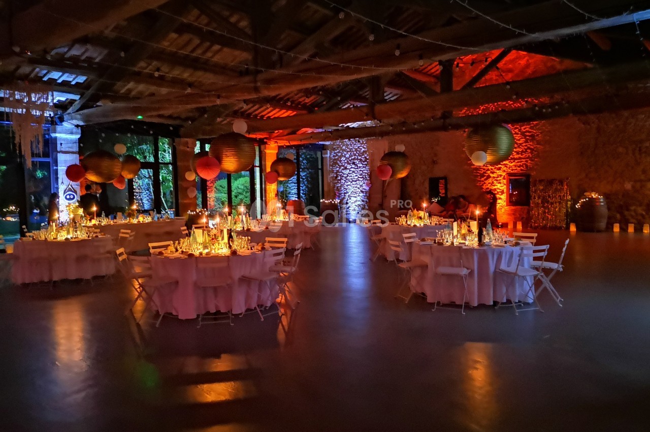 Salle de réception décorée avec des tables rondes, des guirlandes lumineuses et des lanternes suspendues dans une ambiance…