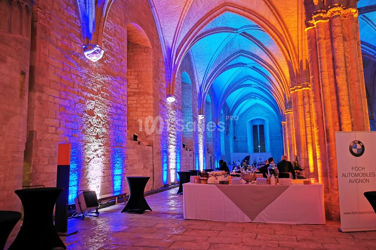 Salle voûtée illuminée en bleu et orange, avec tables de réception et un panneau publicitaire BMW.