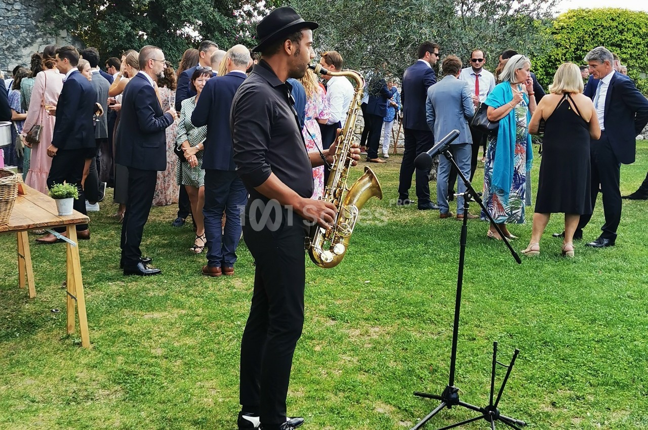 Un musicien jouant du saxophone lors d'un événement en plein air, entouré de personnes discutant.
