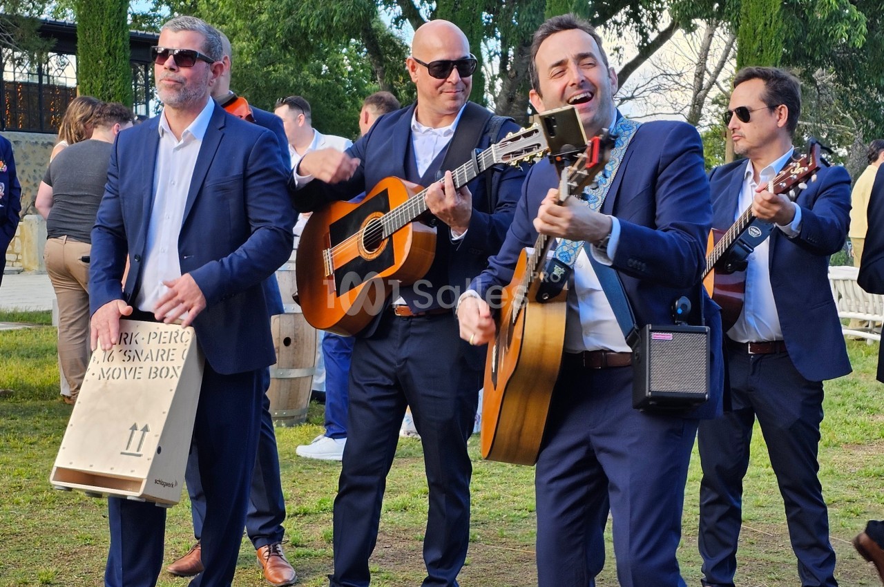 Quatre musiciens en costume jouent de la guitare et du cajón en extérieur lors d'un événement.