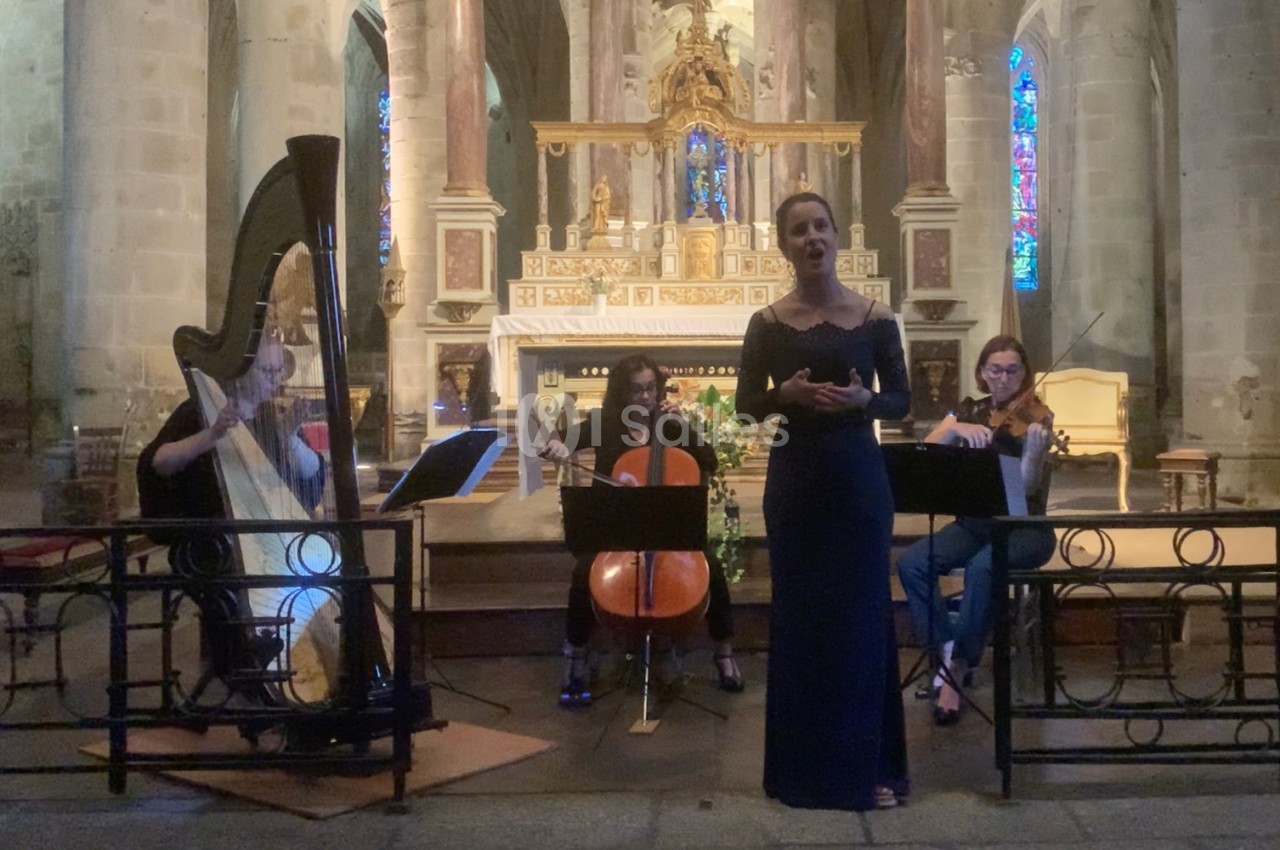 Une chanteuse et trois musiciens (harpe, violoncelle, violon) jouent dans une église devant un autel illuminé.