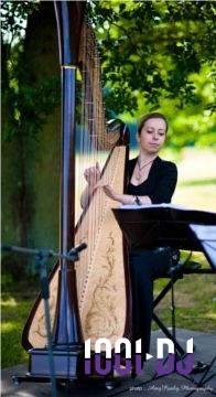 Une musicienne joue de la harpe en plein air, sous un arbre, avec une partition posée devant elle.