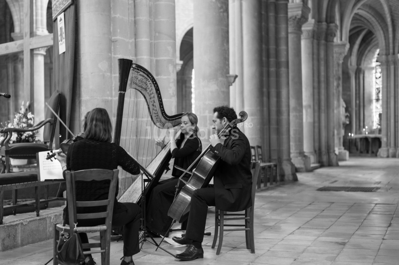 Trois musiciens jouent de la harpe, du violoncelle et d'un autre instrument dans une église aux colonnes imposantes.