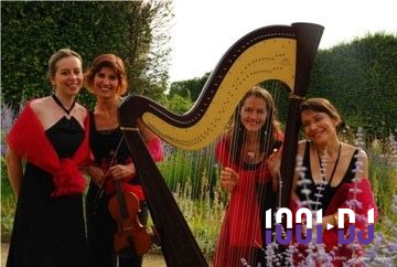 Quatre musiciennes en robes élégantes posent avec une harpe et un violon dans un jardin verdoyant.