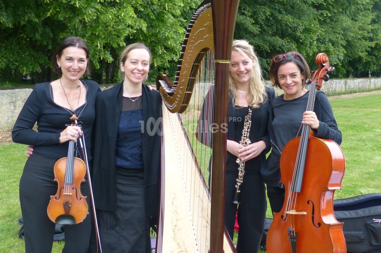 Quatre musiciennes posent avec leurs instruments (violon, harpe, hautbois, violoncelle) dans un parc verdoyant.